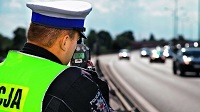 Zdjęcie kolorowe. Umundurowany policjant mierzy prędkość poruszających się pojazdów