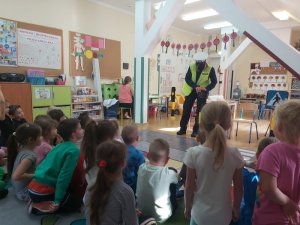 Zdjęcie kolorowe. W sali przedszkola na spotkaniu policjantka prezentuje dzieciom znaki drogowe