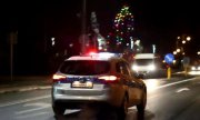 Zdjęcie kolorowe. W nocy policyjny radiowóz jedzie ulicą. W oddali widać światła innego pojazdu