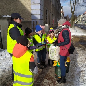 Zdjęcie kolorowe. Policjantka i dzieci ubrane w kamizelki odblaskowe rozmawiają z seniorami na ulicach Szczecinka