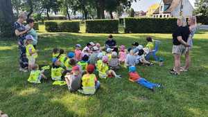 Zdjęcie kolorowe. Policjantka siedzi na trawie wśród dzieci, którym czyta książkę