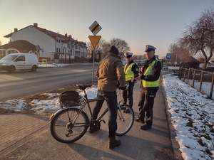 Zdjęcie kolorowe. Policjanci rozdają opaski odblaskowe pieszym i rowerzystom