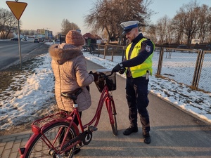 Zdjęcie kolorowe. Policjanci rozdają opaski odblaskowe pieszym i rowerzystom
