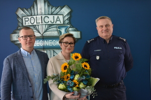 Zdjęcie kolorowe. Zdjęcie Komendanta Powiatowego oraz właścicieli okradzionej firmy, Stojąca w środku kobieta trzyma bukiet kwiatów.