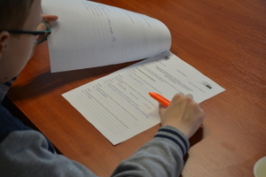 Zdjęcie kolorowe. Uczeń siedzi nad kartką z testem. W dłoni trzyma pomarańczowy długopis