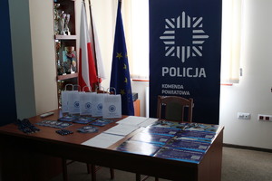 Zdjęcie kolorowe. Na stole leżą poukładane materiały informacyjne zostań policjantem w tle baner szczecineckiej komendy
