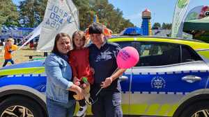 Zdjęcie kolorowe. Policjantka z różowym balonem pozuje do zdjęcia z mamą trzymającą córeczkę na rękach