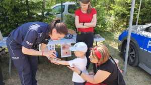 Zdjęcie kolorowe. Policjantka przybija pieczątkę dziecku na rączce