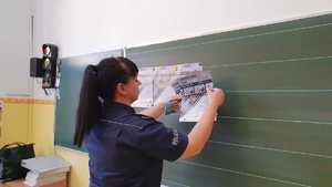 Zdjęcie kolorowe. Policjantka na tablicę magnesami przypina plakaty konkursu &quot;Artystyczny przewodnik&quot;