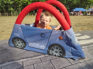 Zdjęcie kolorowe.  Chłopiec siedzi w niebieskim autochodziku z napisem policja