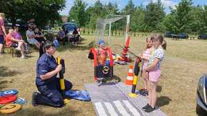 Zdjęcie kolorowe. Policjanta bawi się z dziećmi wykorzystując elementy miasteczka ruch drogowego