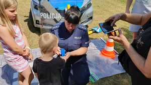 Zdjęcie kolorowe. Policjantka przybija chłopcu na rączkę pieczątkę, wokół stoją inne dzieci
