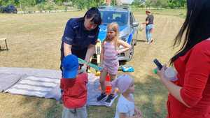 Zdjęcie kolorowe. Policjantka wręcza dzieciom elementy odblaskowe