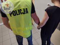 Zdjęcie kolorowe. Policjant w kamizelce odblaskowej z napisem policja. Obok stoi kobieta ubrana na czarno