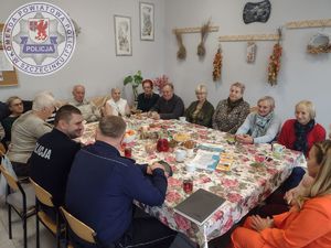 Zdjęcie kolorowe. Przy wspólnym dużym stole siedzą seniorzy oraz umundurowani policjanci