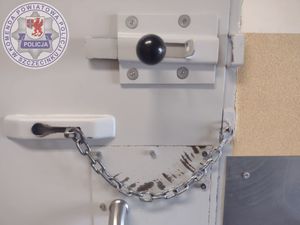 Zdjęcie kolorowe. Widok zabezpieczenia metalowych drzwi w postaci zasuwy i metalowego łańcucha