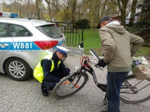 Policjant montuje światełka odblaskowe w rowerze rowerzysty w beżowej kurtce