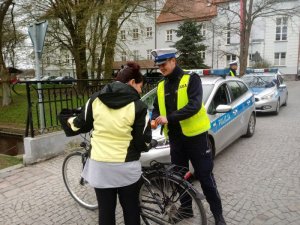 Policjant pokazuje rowerzystce światełka odblaskowe do umieszczenia ich pomiędzy szprychami roweru