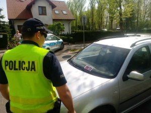Zdjęcie kolorowe: Policjant stoi przy źle zaparkowanym pojeździe.