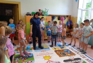 Zdjęcie kolorowe. Policjantka z uczestnikiem gry stoi na wielkoformatowej grze. Wokół zebrane są dzieci.