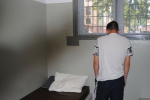 Zdjęcie kolorowe. Mężczyzna odwrócony plecami stoi w celi