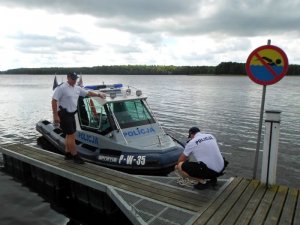 Zdjęcie kolorowe. Policjanci z patrolu wodnego cumują łódź do pomostu.