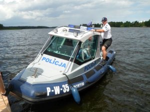 Zdjęcie kolorowe. Na podpływającej do pomostu łodzi widać policjanta przygotowującego się do jej opuszczenia.