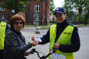 Zdjęcie kolorowe. Policjantka wręcza rowerzystce gadżet odblaskowy