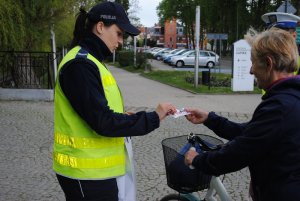 Zdjęcie kolorowe. Policjantka wręcza rowerzystce gadżet odblaskowy