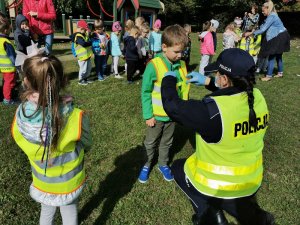 Zdjęcie kolorowe. Policjantka ubiera przedszkolakowi kamizelkę odblaskową