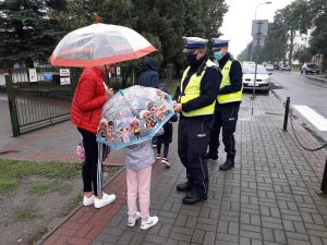 Zdjęcie kolorowe. Policjanci ruchu drogowego wręczają dzieciom odblaski