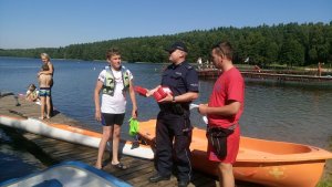 Zdjęcie kolorowe. Policjant na plaży rozmawia z dziećmi