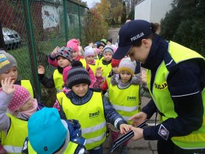 Zdjęcie kolorowe. Policjantka rozdaje elementy odblaskowe