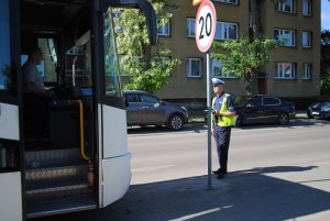 Zdjęcie kolorowe. Policjant ruchu drogowego sprawdza stan techniczny autobusu.