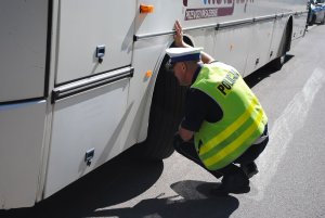 Zdjęcie kolorowe. Policjant ruchu drogowego sprawdza stan techniczny autobusu.