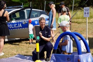 Zdjęcie kolorowe. Policjantka prezentuje dzieciom miasteczko ruchu drogowego