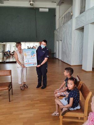 Zdjęcie kolorowe. Policjantka razem z opiekunem grupy trzyma w ręku plakat Bezpiecznie nad wodą