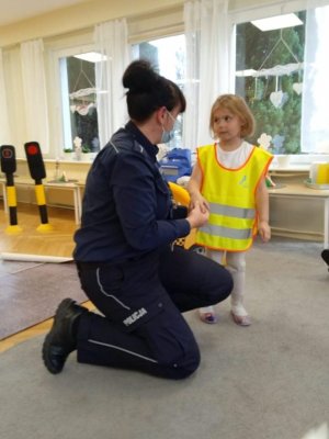 Zdjęcie kolorowe. Policjantka ubiera kamizelkę odblaskową dziewczynce