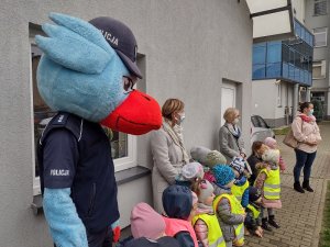 Zdjęcie kolorowe. Gryfuś z dziećmi słucha prelekcji policjantów