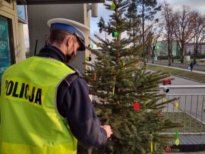 Zdjęcie kolorowe. Policjanci ubierają choinkę w elementy odblaskowe przed wejściem do Komendy Powiatowej Policji w Szczecinku