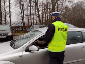 Zdjęcie kolorowe. Policjant przeprowadza kontrolę pojazdu.