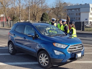 Zdjęcie kolorowe. Policjanci stoją przy zatrzymanym do kontroli drogowej niebieskim samochodzie