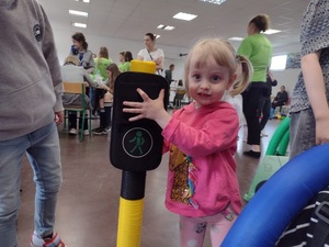 Zdjęcie kolorowe. Mała dziewczynka trzyma w ręku piankowy sygnalizator i pokazuje zielony kolor światła