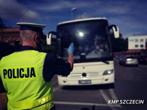 Zdjęcie kolorowe. Policjant ruchu drogowego pokazuje kierowcy autobusu znak do zatrzymania się