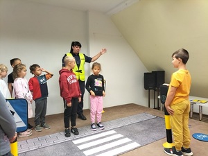 Zdjęcie kolorowe. Policjantka z dziećmi ćwiczy prawidłowe przechodzenie przez przejście dla pieszych