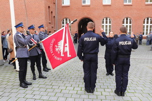 Zdjęcie kolorowe. Ślubowanie policjantów. Z lewej strony stoi poczet sztandarowy z opuszczonym sztandarem. Po prawej stronie 4 policjantów składa ślubowanie