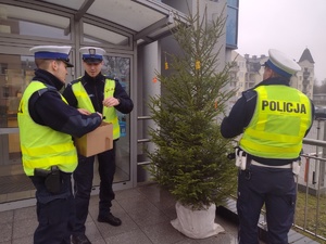 Zdjęcie kolorowe. Policjanci ubierają choinkę w elementy odblaskowe.