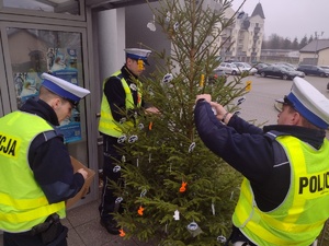 Zdjęcie kolorowe. Policjanci ubierają choinkę w elementy odblaskowe.