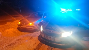 Zdjęcie kolorowe. Zdjęcie zrobione nocą.  Z lewej strony stoi samochód marki VW obok niego z prawej strony oznakowany radiowóz. Policyjny pojazd ma włączone sygnały błyskowe koloru niebieskiego