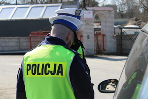 Zdjęcie kolorowe. Policjant dokonuje kontroli pojazdu